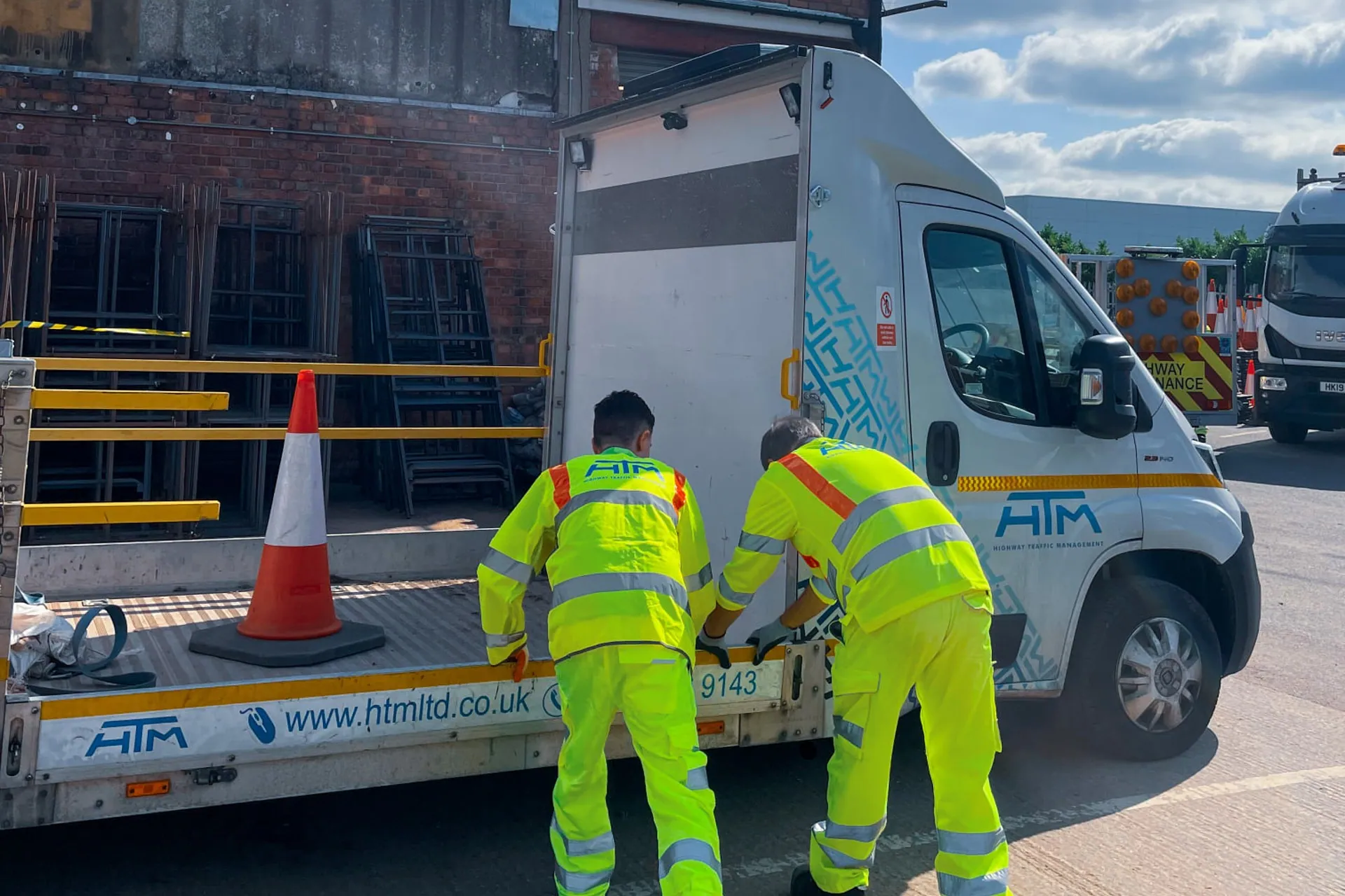 Highway Traffic Management employees in fluorescent uniform beside a branded truck